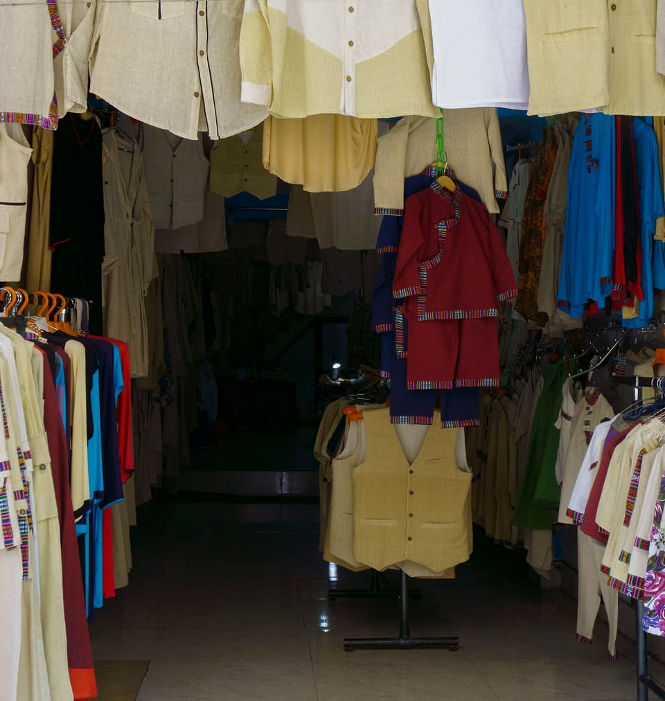 A small clothing shop with shirts and jackets hung from the ceiling