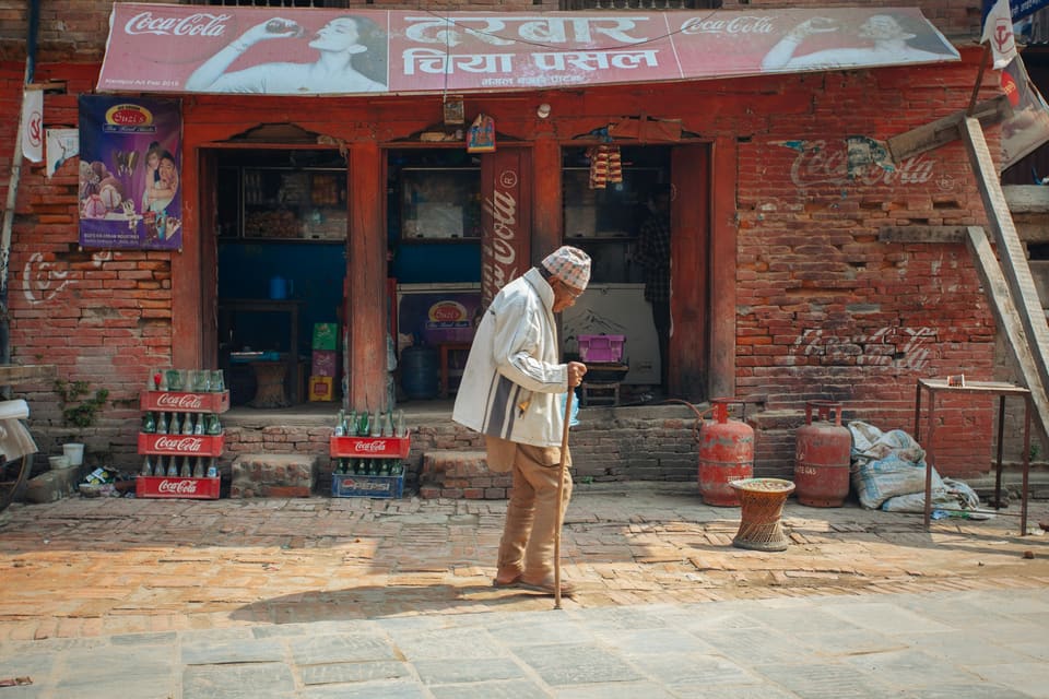 An older man walking past a brick shopfront in Kathmandu