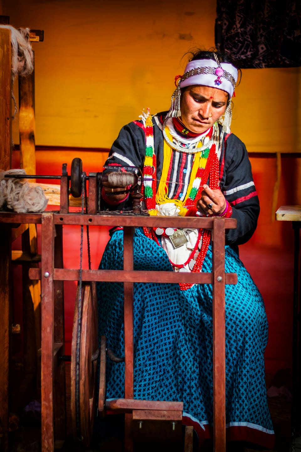 A woman in traditional dress spinning yarn on a wooden wheel