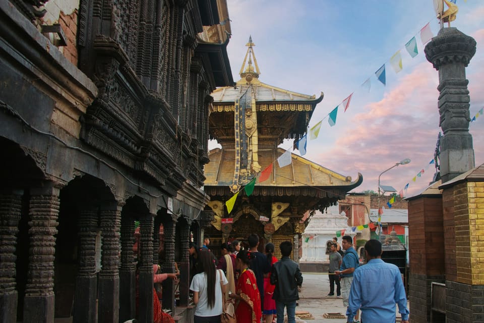 People walking down an old street towards a temple strung with prayer flags