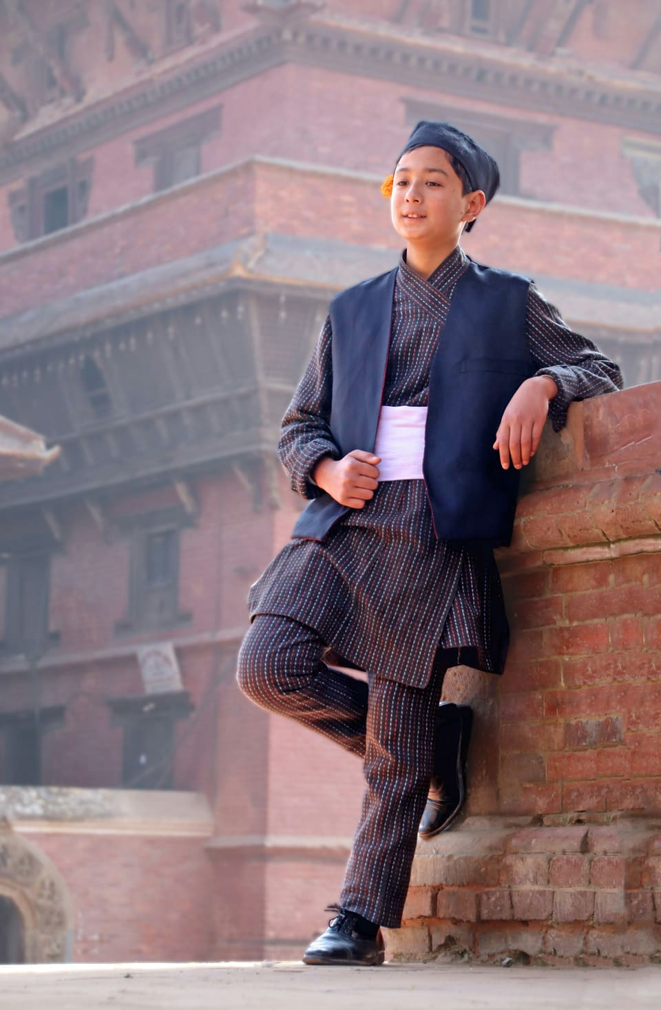 A young man in traditional dress leaning on an old brick wall